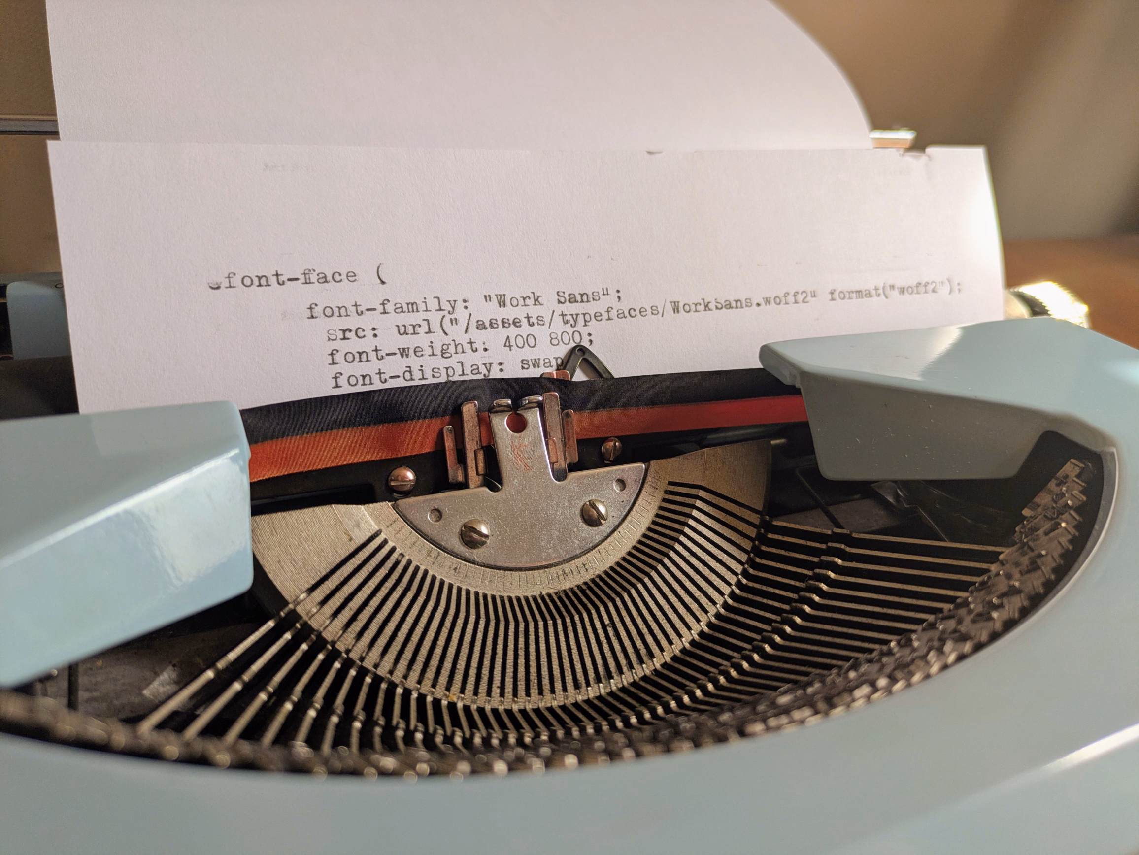 A close-up of paper in a typewriter showing a CSS font-face declaration.