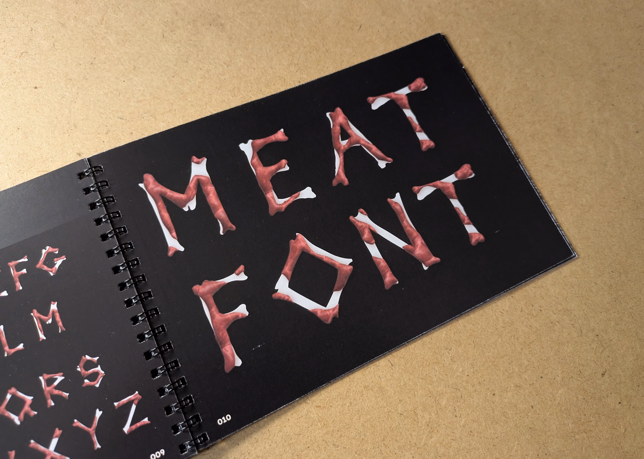 A page showing my meat font, a bony typeface with muscle attached. The words 'Meat Font' are written, and on a page falling out of the crop are a collection of all the glyphs.